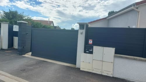 Gated entrance with dark metal gates and white pillars at Résidence des Sables in Mably, France