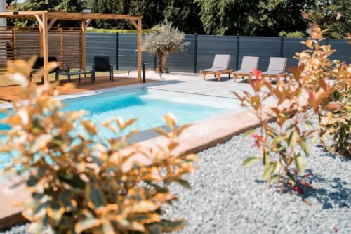 Swimming pool with lounge chairs at Résidence des Sables in Mably, France, surrounded by landscaping and wooden pergola