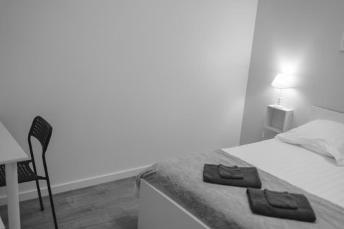 Minimalist bedroom at Résidence des Sables Paris Apartment with bed, black chair, bedside lamp, and hardwood flooring