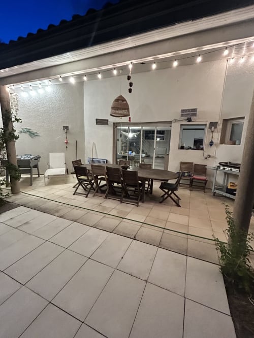 Terrasse de villa moderne la nuit avec table à manger, chaises, guirlandes lumineuses et portes-fenêtres près de la plage de La Teste-de-Buch