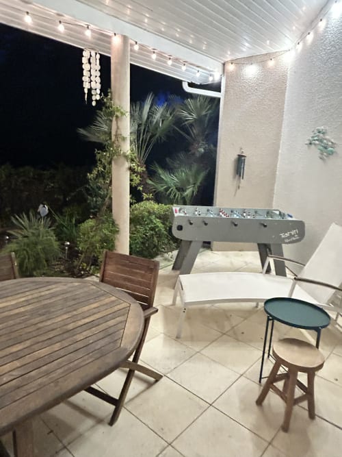 Terrasse de villa moderne à La Teste-de-Buch avec baby-foot, chaises de salle à manger, vue sur le jardin et guirlandes lumineuses