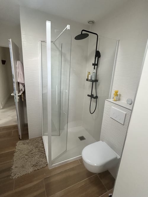 Salle de bain de villa moderne avec douche à l'italienne, pomme de douche effet pluie noire, toilettes blanches et murs carrelés