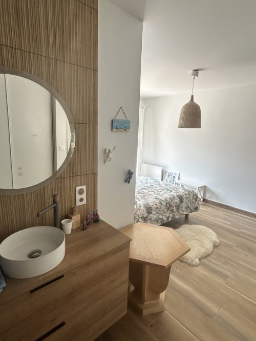 Chambre de villa moderne avec lavabo intégré, miroir rond, finitions bois, suspension luminaire et lit donnant sur le jardin