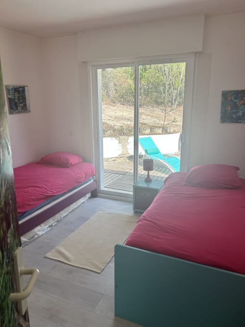 Chambre lumineuse avec deux lits roses et portes vitrées donnant sur le jardin et la piscine de la villa à La Teste-de-Buch