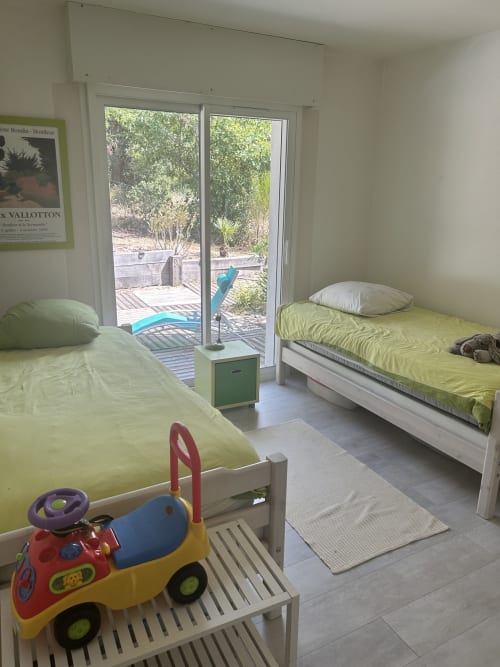 Chambre d'enfants lumineuse de la villa de La Teste-de-Buch avec deux lits, voiture jouet, vue sur le jardin par portes vitrées et accès piscine