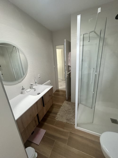 Salle de bains moderne à la villa Dream Properties à La Teste-de-Buch avec lavabo blanc, miroir rond, douche vitrée et