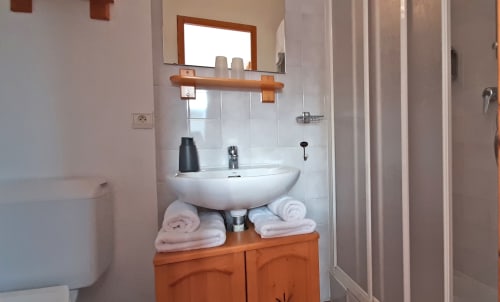 Salle de bain avec lavabo blanc sur piédestal, meuble en bois, miroir et serviettes blanches au Chalet De La Yodine