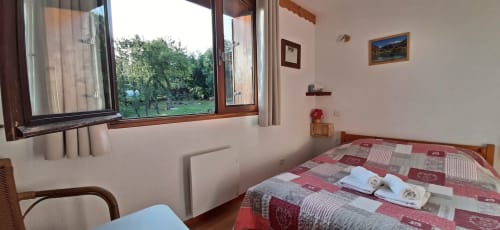 Chambre double douillette au Chalet De La Yodine avec literie patchwork rouge, vue montagne par grandes fenêtres, et privée
