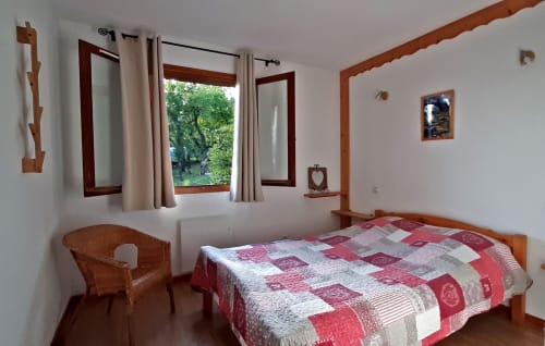 Chambre double confortable au Chalet De La Yodine avec vue montagne, mobilier en bois, courtepointe patchwork et fauteuil en rotin.