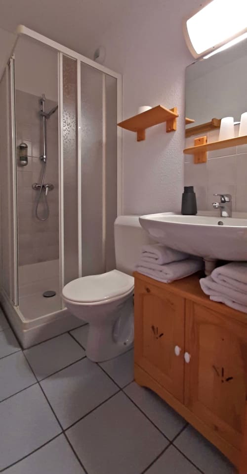 Salle de bain moderne au Chalet De La Yodine avec douche à l'italienne, lavabo blanc, meuble vasque en bois et sèche-serviettes électrique