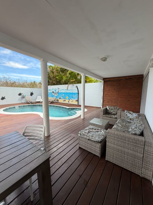 Terrasse couverte avec mobilier en rotin, vue sur la piscine et fresques tropicales à la villa La Case à Nath, Saint-Pierre Réunion