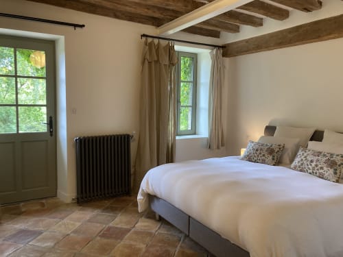 Chambre lumineuse au Gîte Le Jardin de Marie à Sancerre avec poutres apparentes, lit blanc, vue sur le jardin et radiateur vintage