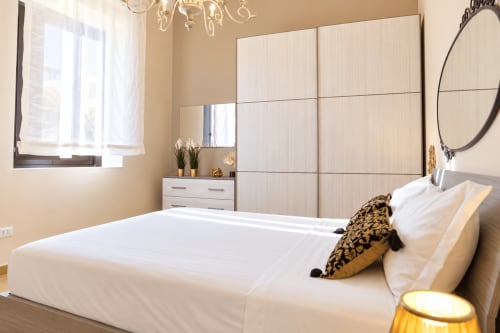 Modern bedroom in Catania apartment with white bed, leopard print pillow, sliding wardrobe, city view window, and elegant