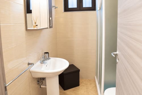 Modern bathroom with pedestal sink, mirror, beige tile walls in Catania apartment