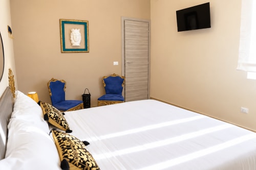 Luxury bedroom at Sicily In Home apartment in Catania with blue velvet chairs, flat-screen TV, and white bedding