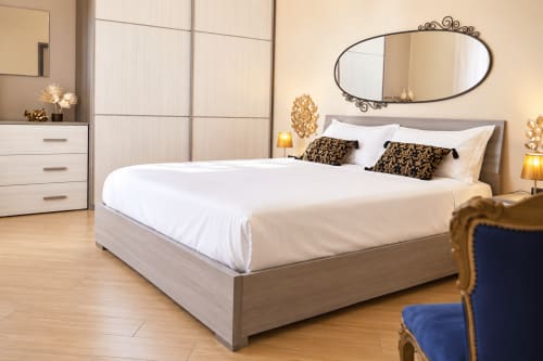 Elegant Sicilian apartment bedroom with white linens, wooden bed, ornate mirror, beige walls, and furnished with modern