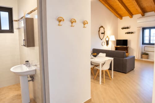 Modern apartment in Catania with open-plan living, white pedestal sink, gray sofa, dining table, wooden beams, and city