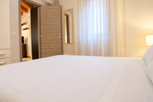 Modern bedroom in Central House Fish Market apartment, Catania Sicily with white bed, wooden door, and city view curtains