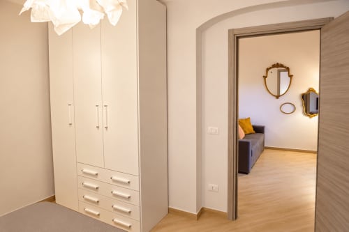 Modern bedroom closet with white wardrobe and drawers in Catania apartment, leading to furnished room with mirrors and