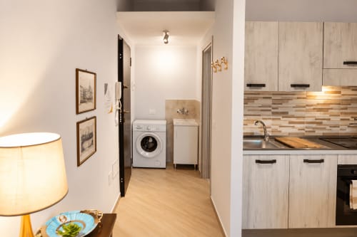 Modern apartment kitchen and laundry area in Catania with wooden cabinetry, washer, and stainless steel appliances