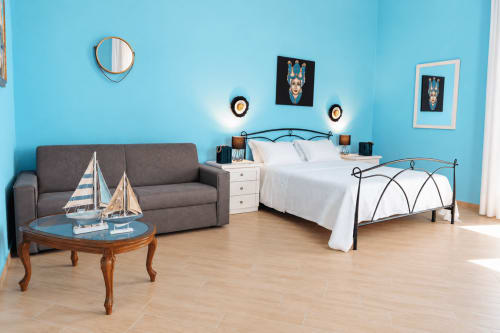 Camera da letto moderna in appartamento a Catania con pareti blu brillanti, letto matrimoniale, divano grigio e tavolo in legno con decorazioni nautiche