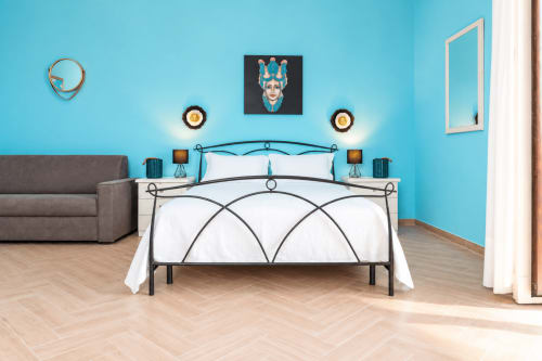 Camera da letto luminosa con letto in metallo, biancheria bianca, testata turchese e divano grigio presso Sicily In Home