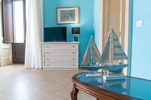Soggiorno azzurro turchese con decorazioni nautiche, comò bianco e TV nell'appartamento In Home di Sicilia