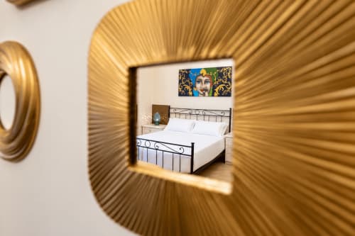 Gold-framed mirror reflecting bedroom with wrought iron bed at Sicily In Home apartment in Catania