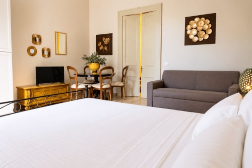 Spacious Catania apartment bedroom with white bed, gray sofa, wooden desk, and gold-toned décor accents
