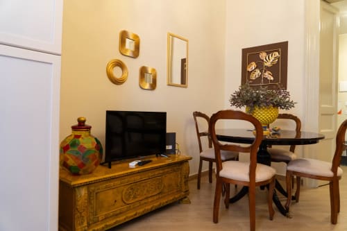 Elegant apartment living room in Catania with flat-screen TV, wooden furniture, and dining area with red chairs