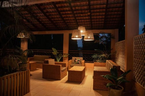 Beachfront terrace lounge at NOMADS EN BORD DE MER, Lomé with woven seating, pendant lights, and tropical plants at dusk