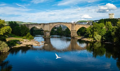 Puente de piedra histórico que cruza un río rodeado de vegetación exuberante cerca del hotel A Casiña D'Avoa en Osera, España
