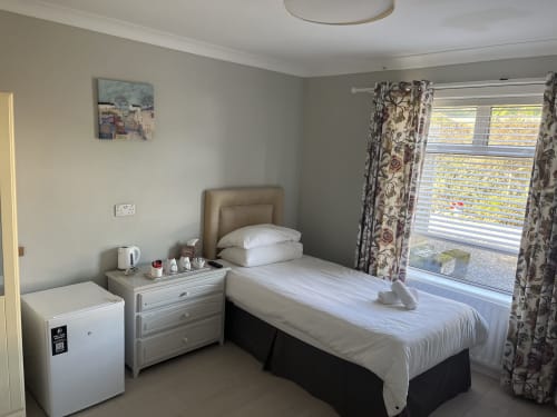 Single room at Coral Gables Guesthouse in Wexford with bed, mini fridge, nightstand, and patterned curtains