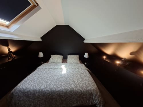 Chambre mansardée moderne aux murs noirs, puits de lumière, lit queen-size et éclairage chaleureux à l'hôtel Love Room Sensation