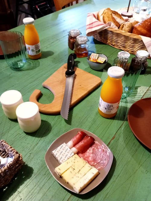 Petit-déjeuner à la Paulusmühle : corbeille de pain, charcuterie, fromage, jus d'orange et condiments sur table verte