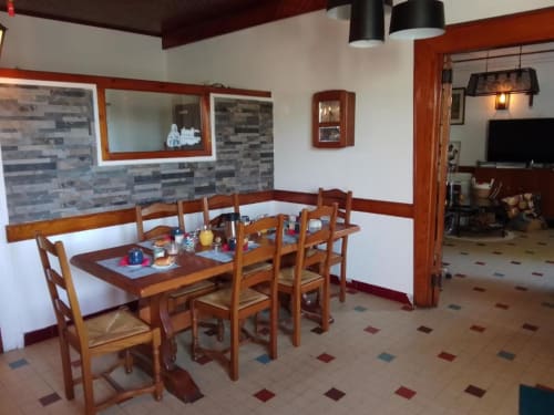 Salle à manger de La Maison de Barlest avec table en bois, chaises, dosseret en pierre et aménagement ouvert
