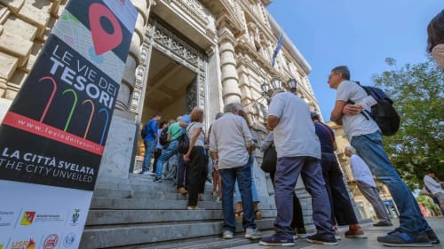 Turisti che entrano in un edificio storico siciliano con il banner della mostra 'Le Vie dei Tesori' a Carini