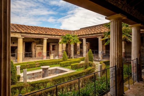 Cortile di Casa Ida a Vietri: colonne romane, fontana centrale, siepi curate e tetto in cotto