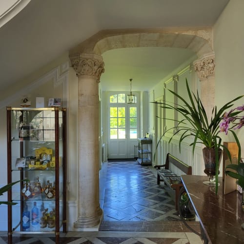 Élégant couloir du Logis des Tourelles B&B à Cognac avec colonnes classiques, orchidées en pots et vitrine