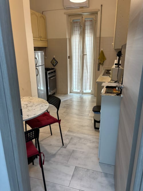 Cucina e zona pranzo moderna nell'appartamento di Ostia con elettrodomestici in acciaio inox, piano in marmo e sedie nere