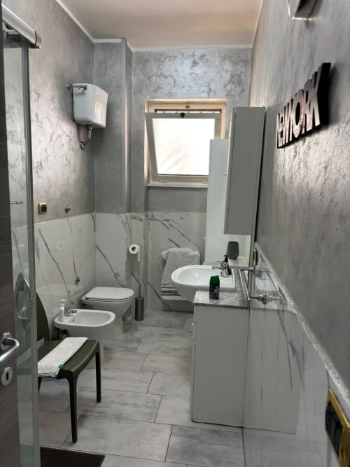 Bagno moderno nell'appartamento ViOletta a Lido di Ostia con piastrelle in marmo, wc, bidet, lavabo, specchio e zona doccia