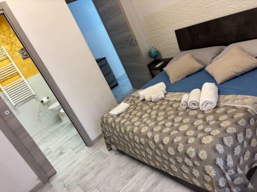 Camera moderna dell'hotel ViOletta a Ostia con biancheria blu, coperta a stampa margherita, asciugamani arrotolati e bagno en-suite