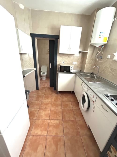 Cocina y baño modernos en apartamento de Jerez con muebles blancos, electrodomésticos de acero inoxidable y piso de baldosas de barro