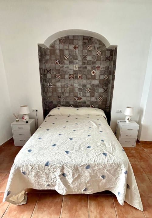 Cama individual con colcha acolchada blanca y cabecero de azulejos en apartamento de Jerez