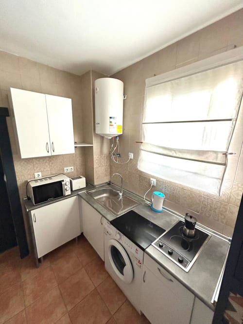 Cocina compacta en apartamento de Jerez con placa de cocción eléctrica, lavadora, microondas y calentador de agua en paredes con azulejos beige