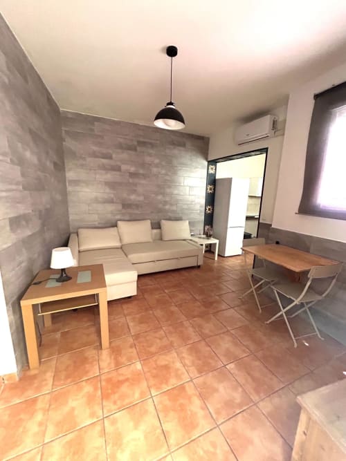 Luminoso salón en apartamento de Jerez con sofá beige, mesa de madera, baldosas de barro y lámpara colgante negra moderna