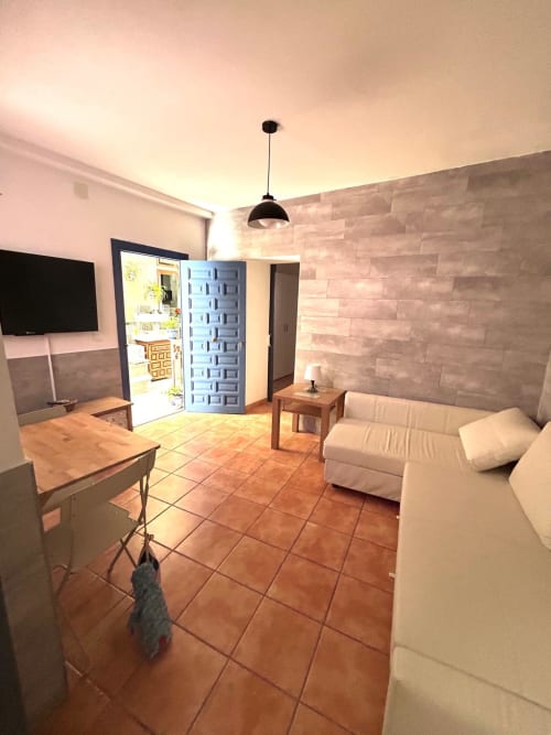Moderno salón en Jerez de la Frontera con sofá beige, televisor, suelo de barro y puerta de entrada azul