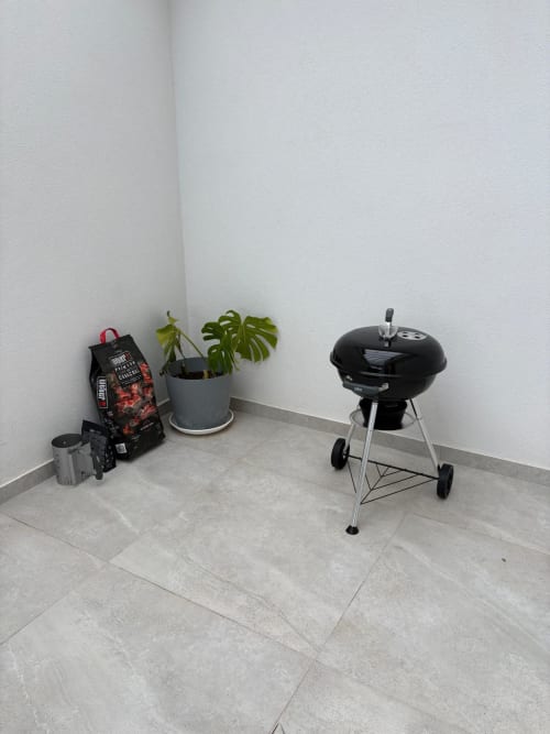 Pátio da villa BHF Residences com churrasqueira de carvão, planta monstera em vaso e utensílios de churrasco no terraço de concreto
