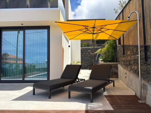 Terraço de villa moderna no BHF Residences com espreguiçadeiras, guarda-sol amarelo e paredes de pedra em Arco da Calheta