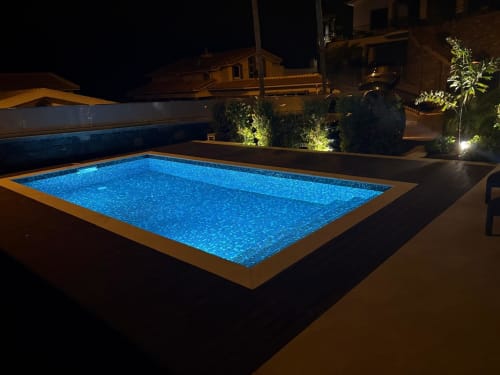 Piscina retangular iluminada à noite com iluminação LED azul, rodeada por terraço na villa BHF Residences em Arco